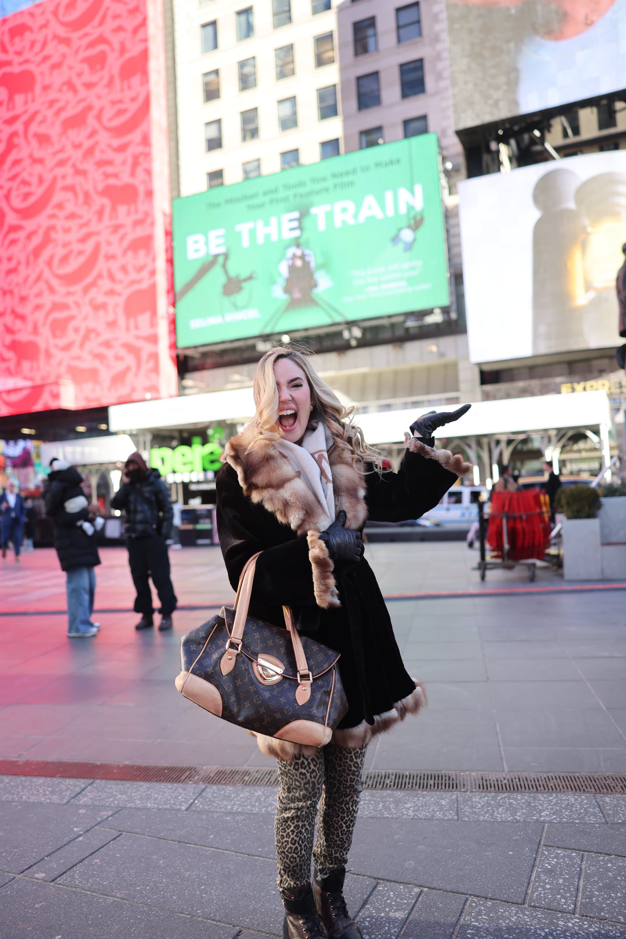 Selina Ringel celebrating beneath a Be The Train billboard in Times Square